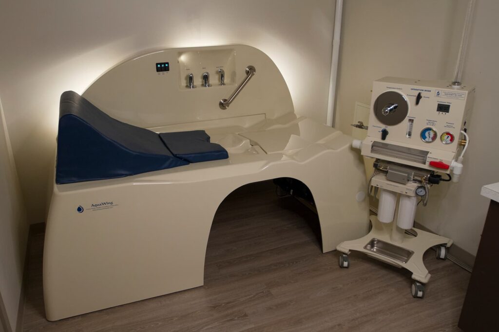 AquaWing CLOSED colon hydrotherapy treatment table with integrated control panel and patient support cushions.