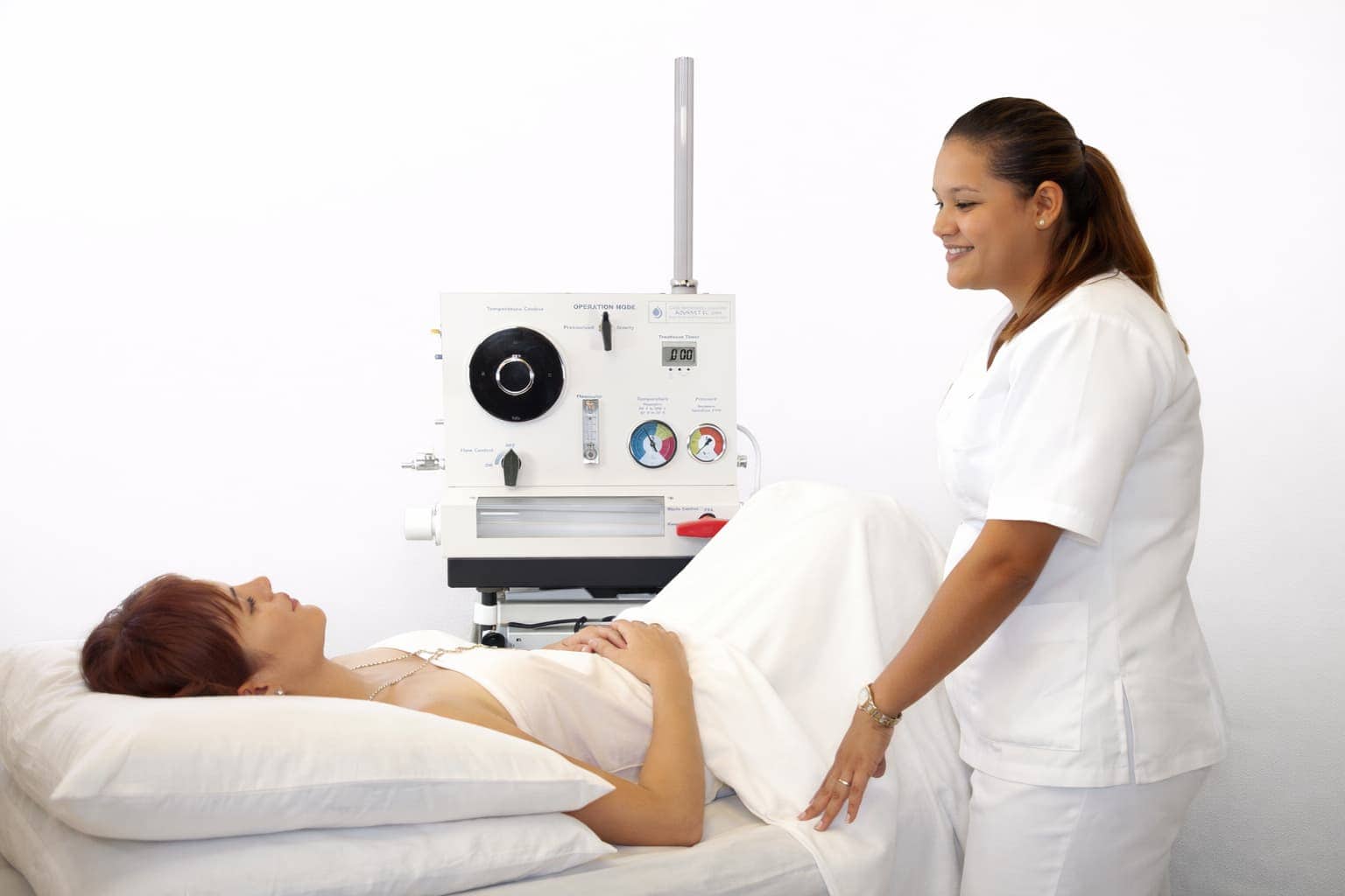 A healthcare professional assists a patient lying on a bed next to a medical device in a clinical setting.